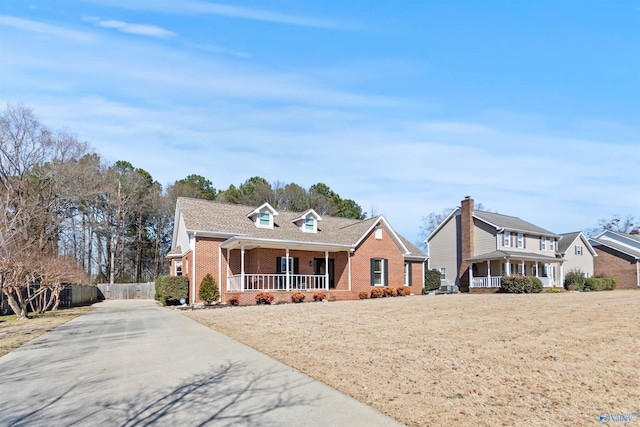 view of front facade featuring covered porch, fence, concrete driveway, and brick siding