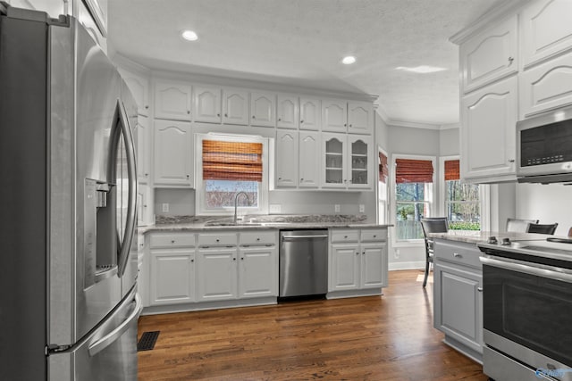kitchen with crown molding, stainless steel appliances, dark wood-type flooring, a sink, and light stone countertops