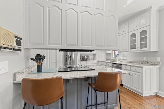kitchen with light stone counters, a breakfast bar, white cabinetry, and a peninsula