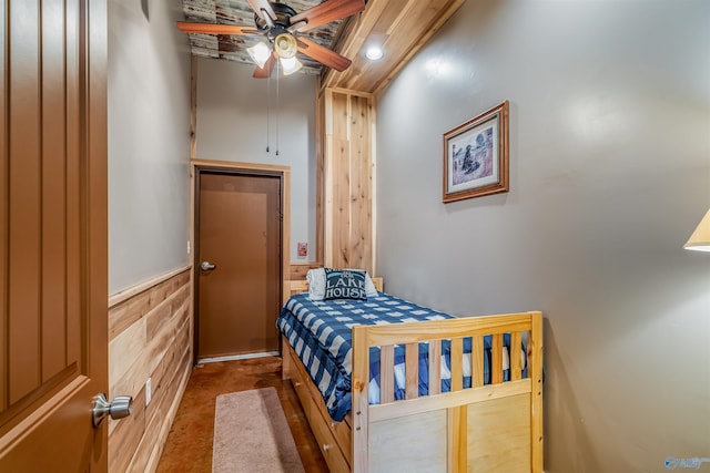 bedroom with a wainscoted wall, wooden walls, and a ceiling fan