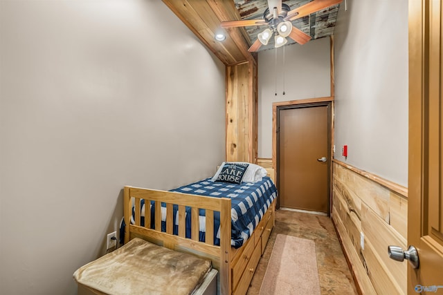 bedroom with a wainscoted wall, wood walls, and a ceiling fan