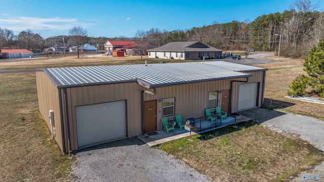 view of front of house with gravel driveway, a detached garage, metal roof, and a front yard