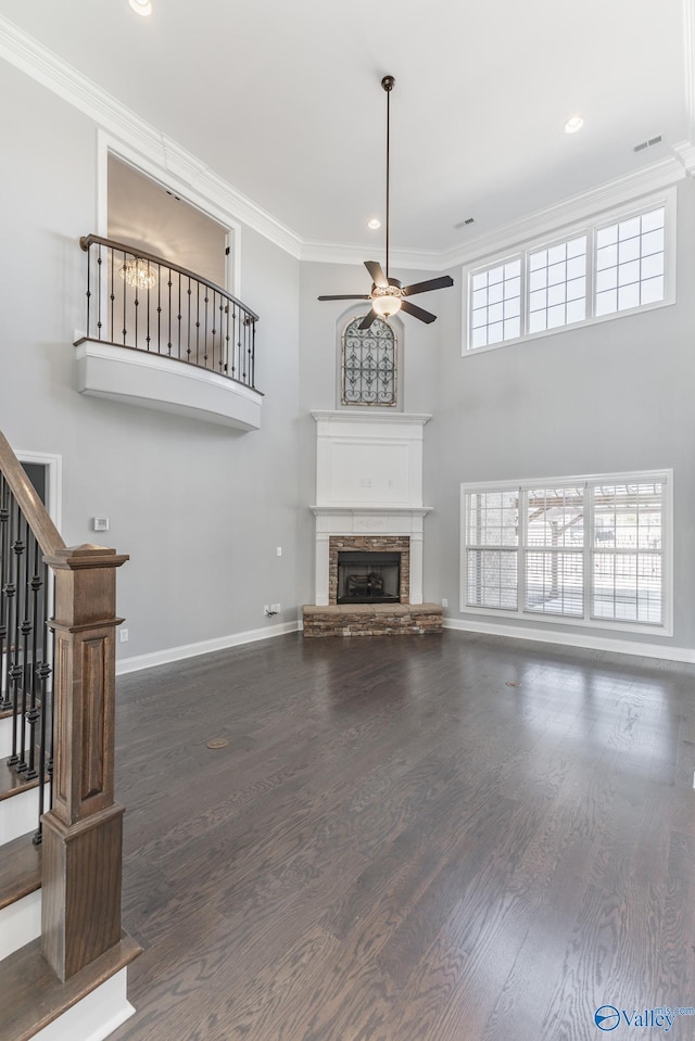 unfurnished living room with a stone fireplace, crown molding, ceiling fan, and dark hardwood / wood-style floors