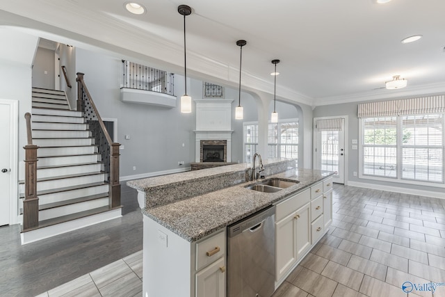 kitchen featuring white cabinets, a stone fireplace, sink, stainless steel dishwasher, and decorative light fixtures