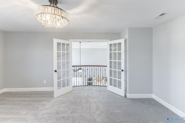 carpeted empty room with french doors and a chandelier