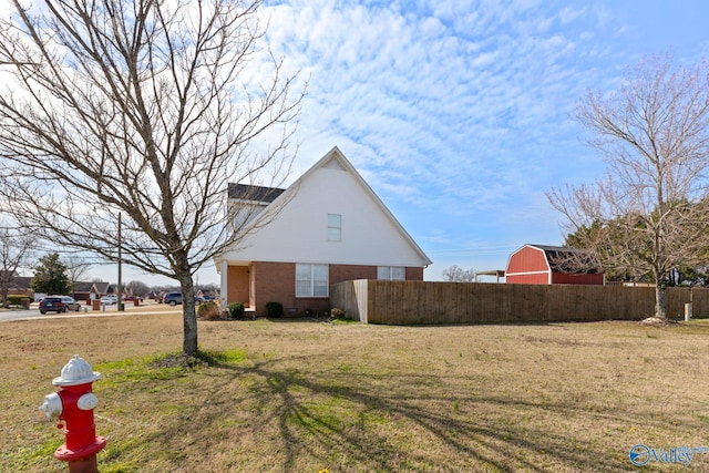 view of home's exterior with a yard, brick siding, a barn, and fence