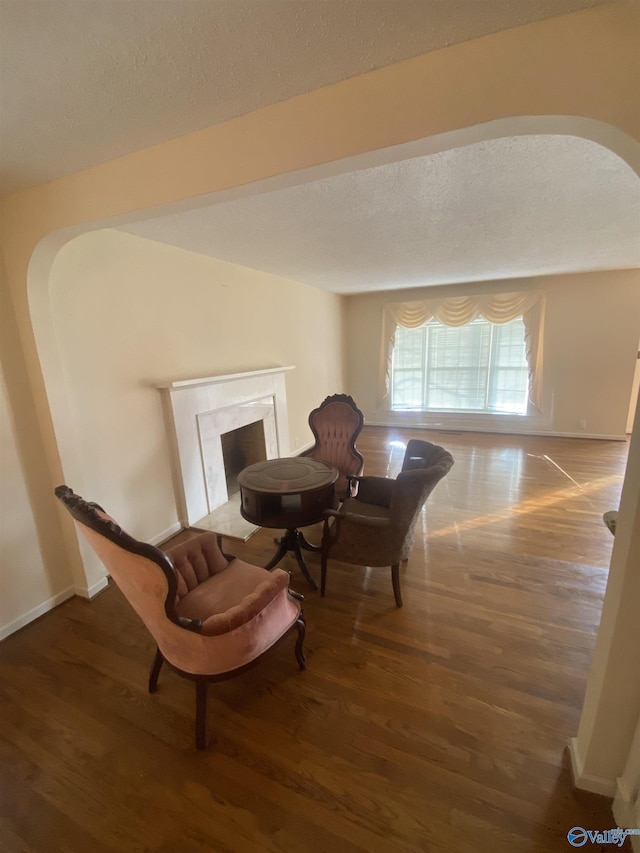 sitting room with a premium fireplace, a textured ceiling, and dark wood-type flooring