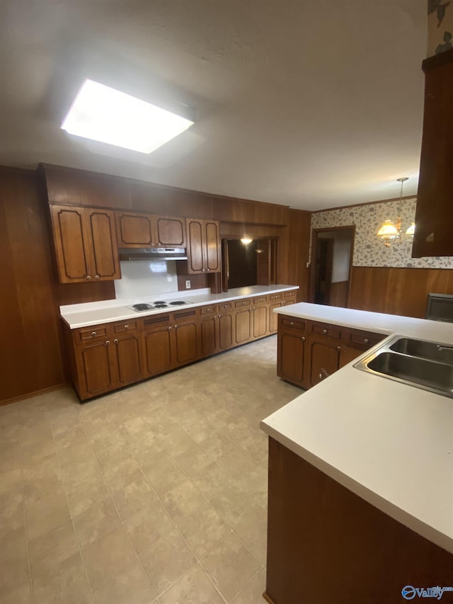 kitchen featuring sink, white electric stovetop, wood walls, and pendant lighting