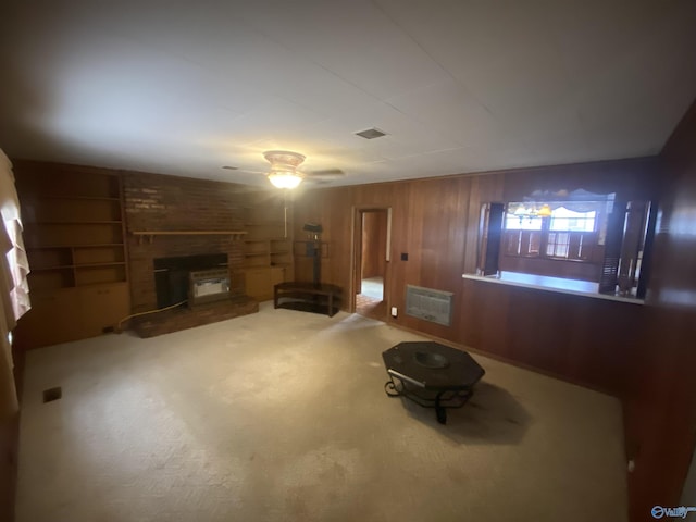 unfurnished living room featuring ceiling fan, carpet floors, wood walls, a brick fireplace, and built in features