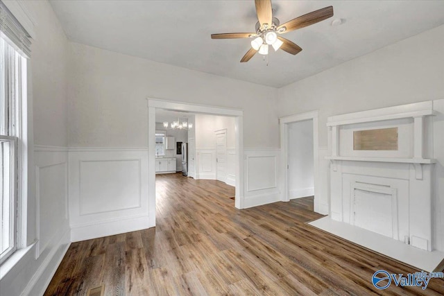 unfurnished living room featuring ceiling fan with notable chandelier and wood-type flooring