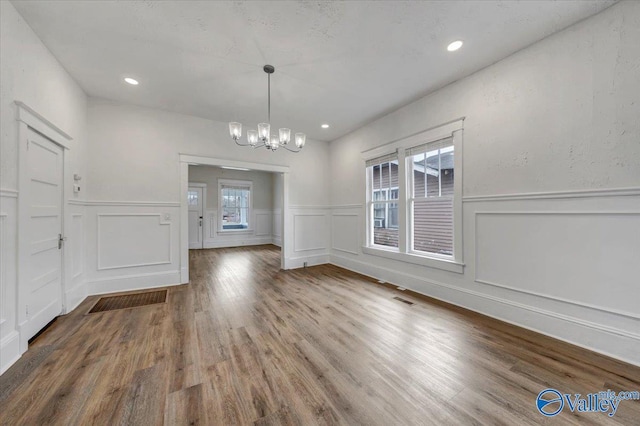 unfurnished dining area with a healthy amount of sunlight, wood-type flooring, and a notable chandelier