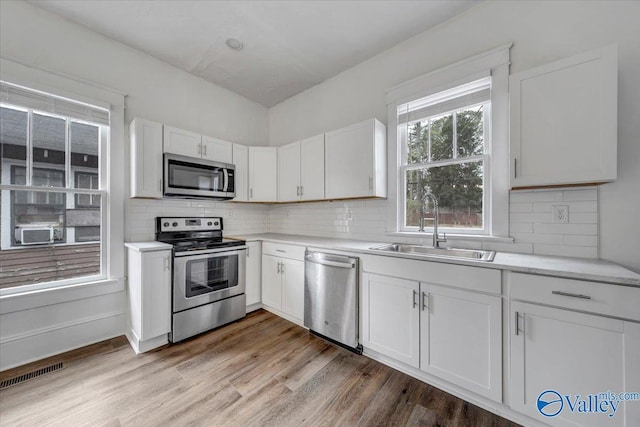 kitchen featuring sink, light hardwood / wood-style flooring, appliances with stainless steel finishes, white cabinets, and backsplash