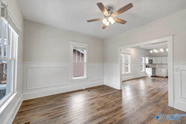 interior space featuring ceiling fan with notable chandelier, dark wood-type flooring, and a healthy amount of sunlight