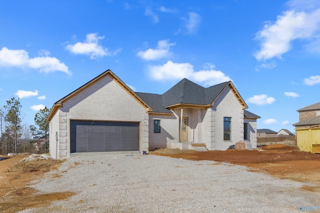 view of front facade featuring an attached garage, gravel driveway, and brick siding