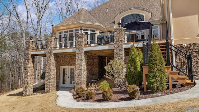 view of front of home with roof with shingles, stucco siding, stairs, french doors, and stone siding