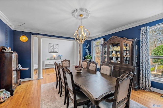 dining space featuring an inviting chandelier, crown molding, light wood-style floors, and decorative columns