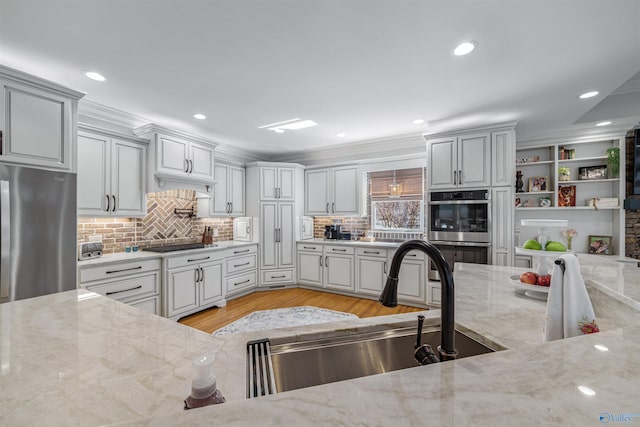 kitchen with light stone countertops, a sink, decorative backsplash, appliances with stainless steel finishes, and light wood-type flooring