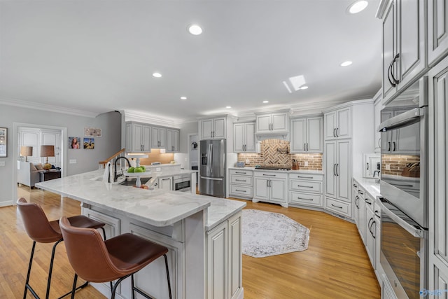 kitchen featuring a breakfast bar area, light wood-style flooring, stainless steel appliances, crown molding, and backsplash