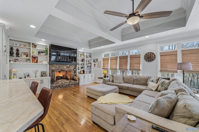 living area featuring light wood-style flooring, a fireplace, a raised ceiling, and crown molding