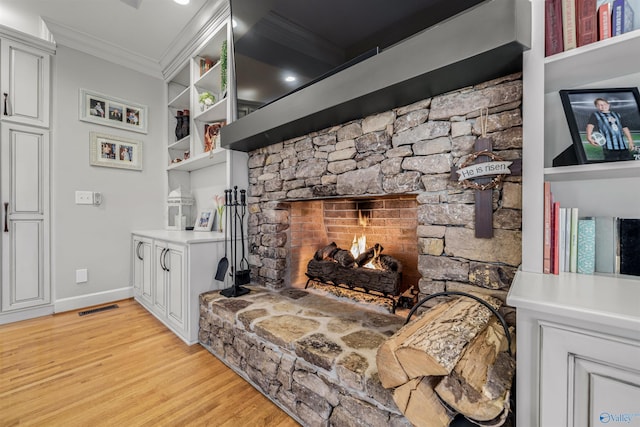 living area featuring visible vents, baseboards, ornamental molding, light wood-style flooring, and a fireplace