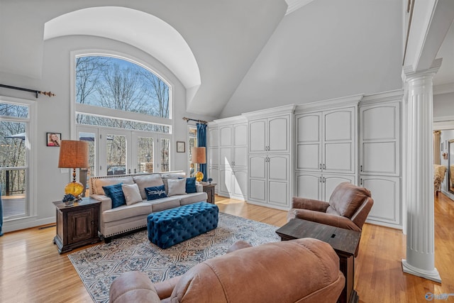 living area featuring decorative columns, light wood-type flooring, a wealth of natural light, and high vaulted ceiling