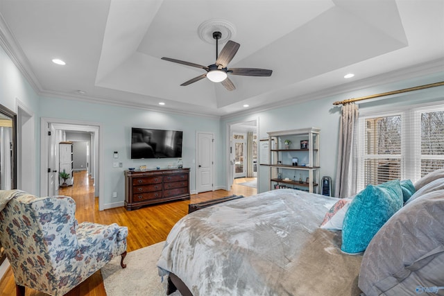 bedroom with baseboards, light wood-type flooring, ornamental molding, recessed lighting, and a raised ceiling