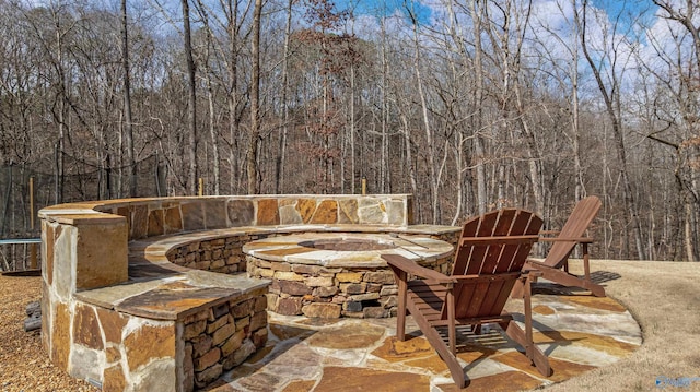 view of patio with a wooded view and an outdoor fire pit