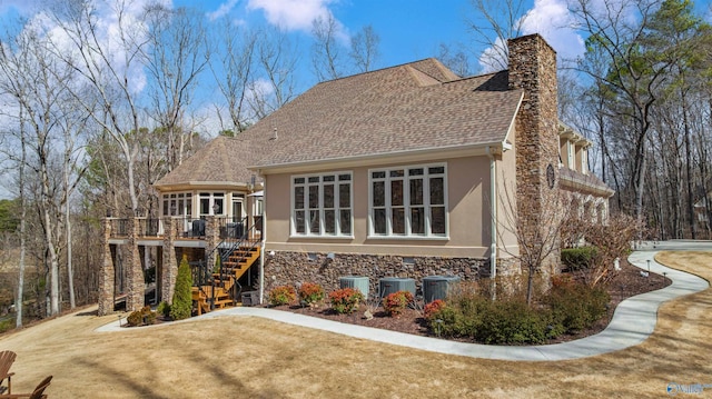 back of house featuring stairs, stucco siding, a lawn, a chimney, and stone siding