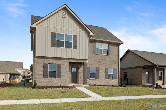 view of front facade with fence, roof with shingles, board and batten siding, a front yard, and brick siding