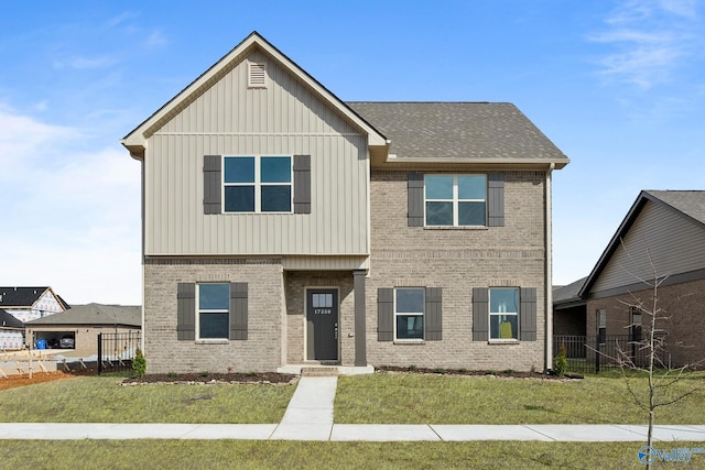 view of front facade featuring brick siding, board and batten siding, a front yard, and fence