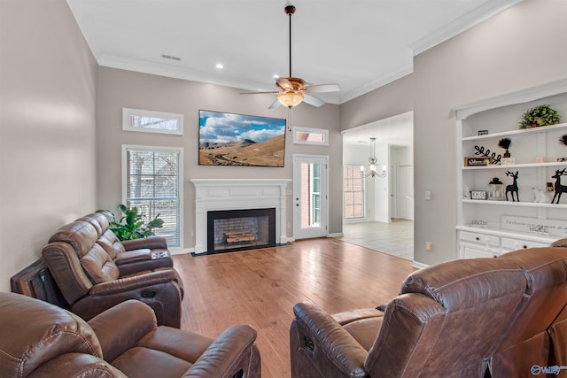 living room featuring light wood finished floors, a fireplace with flush hearth, ornamental molding, and ceiling fan with notable chandelier