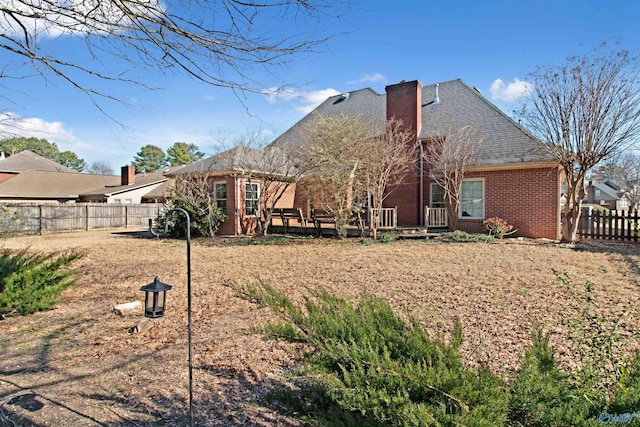 back of property with a deck, brick siding, a chimney, and fence