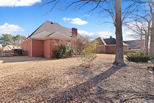 view of side of property with roof with shingles, brick siding, a chimney, and fence