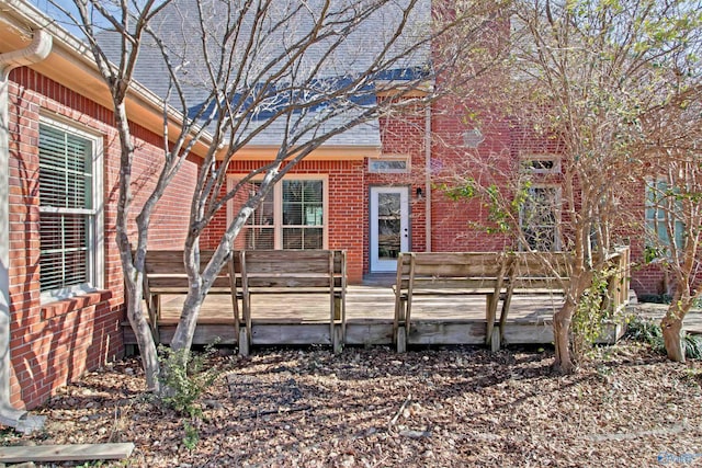 exterior space featuring a deck, brick siding, and a shingled roof