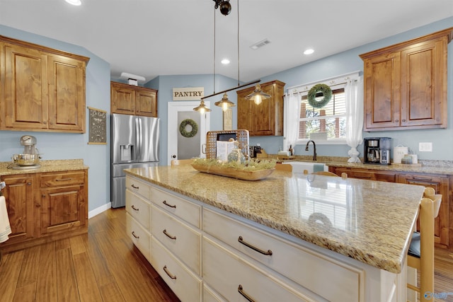 kitchen featuring pendant lighting, sink, light hardwood / wood-style flooring, a kitchen island, and stainless steel fridge with ice dispenser