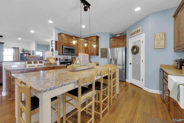 kitchen with appliances with stainless steel finishes, light wood-type flooring, hanging light fixtures, and a breakfast bar area