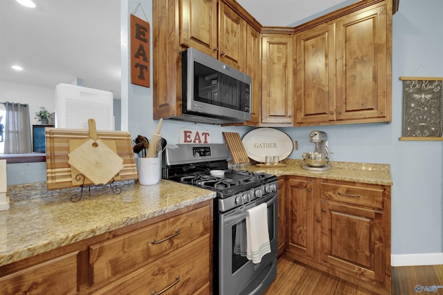 kitchen with light stone countertops, light hardwood / wood-style flooring, and appliances with stainless steel finishes