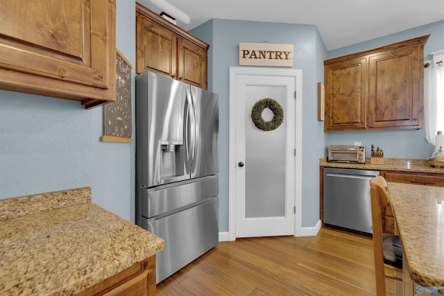 kitchen featuring light stone countertops, stainless steel appliances, and light hardwood / wood-style flooring