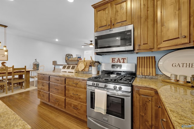 kitchen featuring decorative light fixtures, light stone counters, light wood-type flooring, and stainless steel appliances