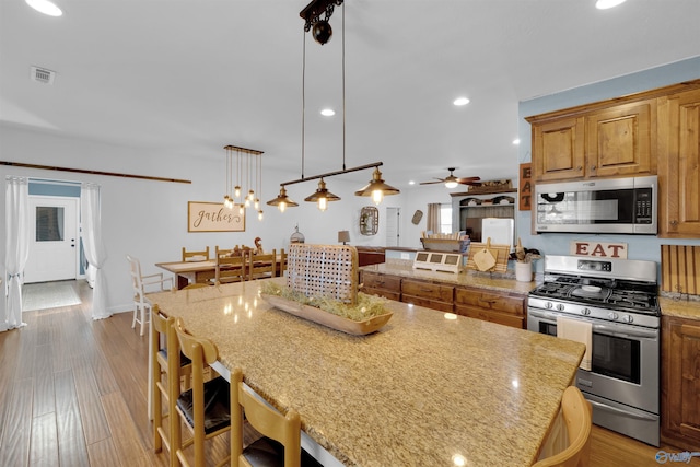 kitchen featuring a breakfast bar, stainless steel appliances, ceiling fan, decorative light fixtures, and light hardwood / wood-style floors