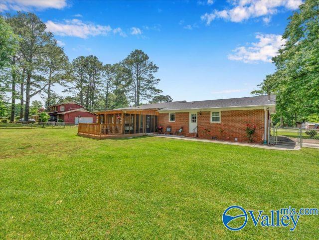 rear view of house with a lawn, fence, a sunroom, and brick siding