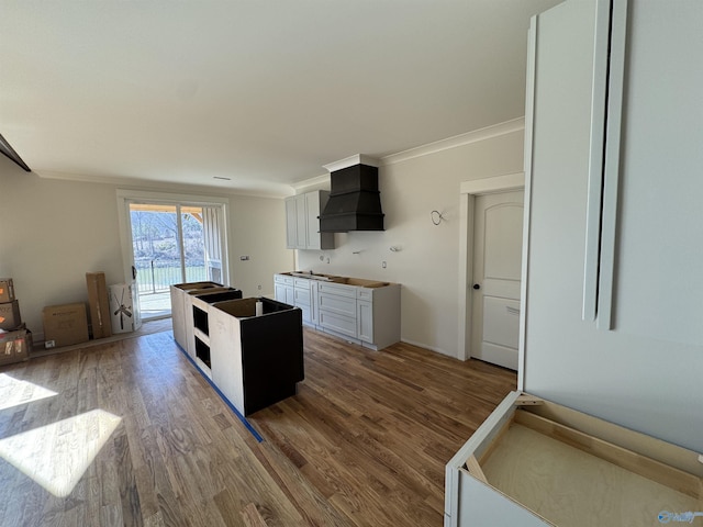 kitchen with white cabinets, custom exhaust hood, ornamental molding, and wood-type flooring