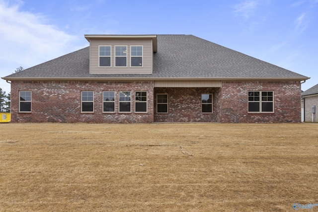 rear view of house with brick siding, a yard, and roof with shingles