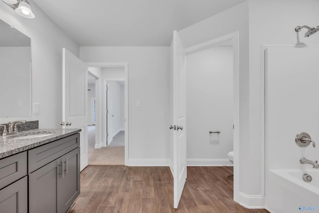 full bath featuring baseboards, toilet, vanity, wood finished floors, and washtub / shower combination