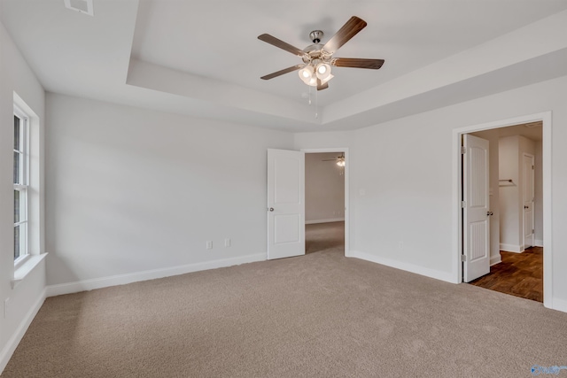 unfurnished bedroom with a ceiling fan, a raised ceiling, baseboards, and dark colored carpet