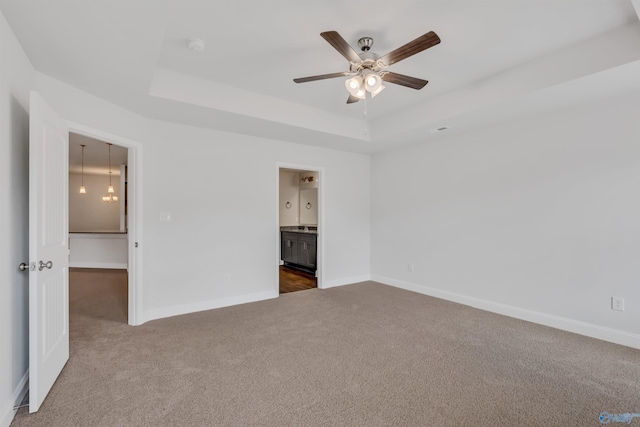 unfurnished bedroom featuring dark colored carpet, baseboards, and a raised ceiling