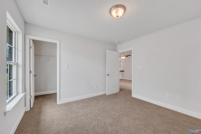 unfurnished bedroom with visible vents, a walk in closet, a closet, carpet floors, and baseboards