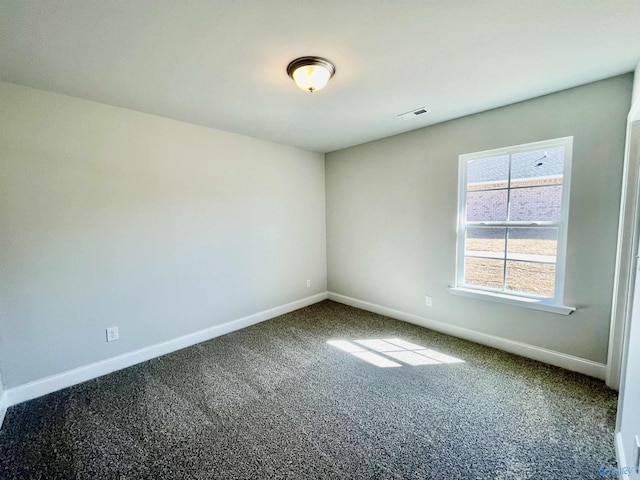 spare room featuring visible vents, baseboards, and dark colored carpet