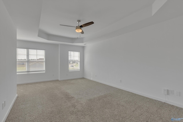 carpeted empty room with ceiling fan and a raised ceiling