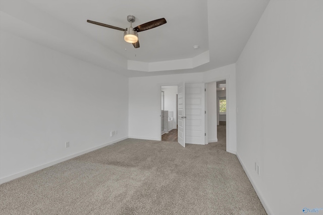 unfurnished bedroom with light carpet, a tray ceiling, and ceiling fan